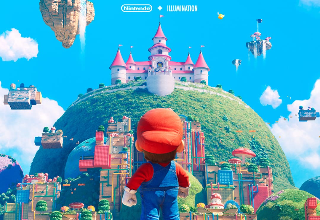 A imagem mostra o Mario olhando para o Castelo da princesa Peach, que está no topo de um morro repleto de referências ao jogo ao redor. A imagem é do novo filme Super Mario Bros