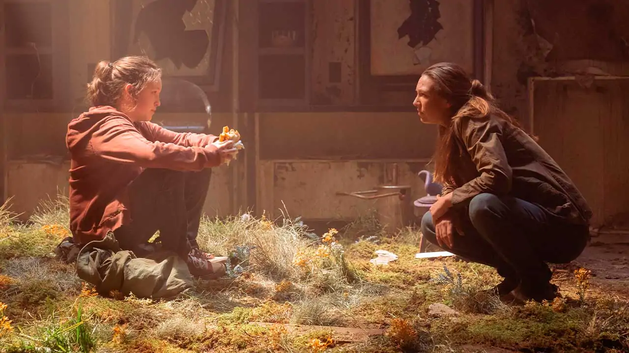 Imagem retirada da série The Last of Us onde mostra Ellie e Sarah se encarando enquanto Ellie come um sanduíche