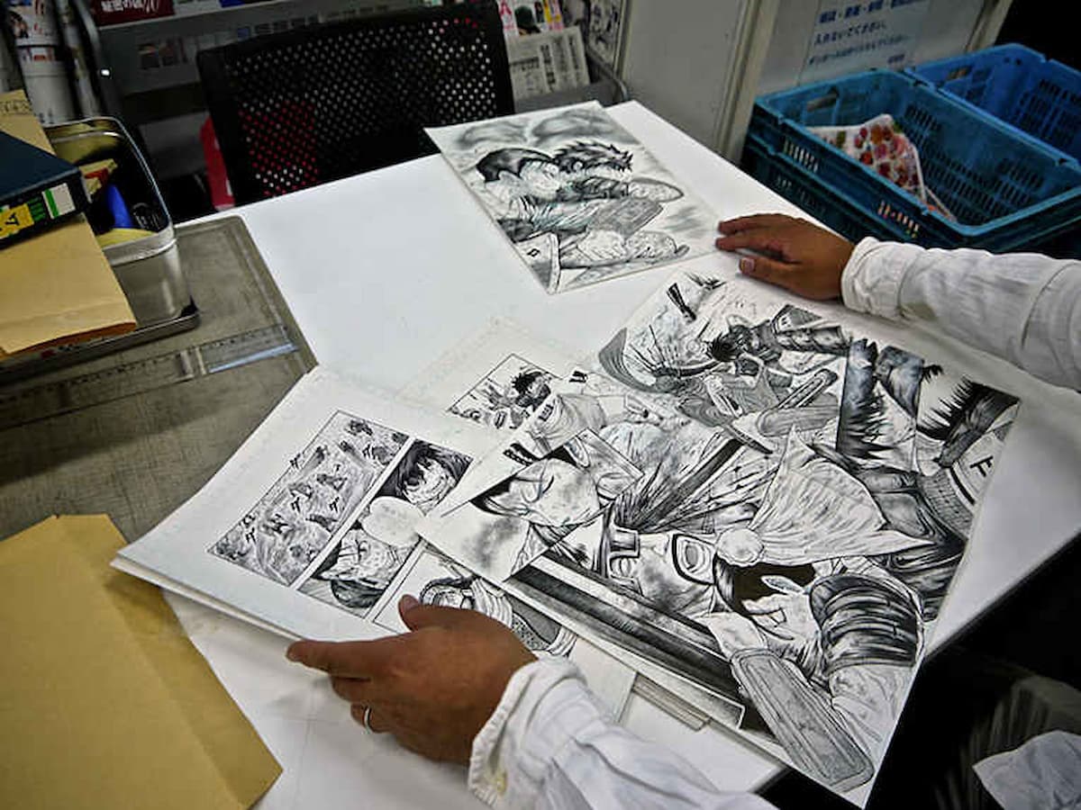 Pessoa pegando em diversos rascunhos de um desenho em anime em uma mesa.