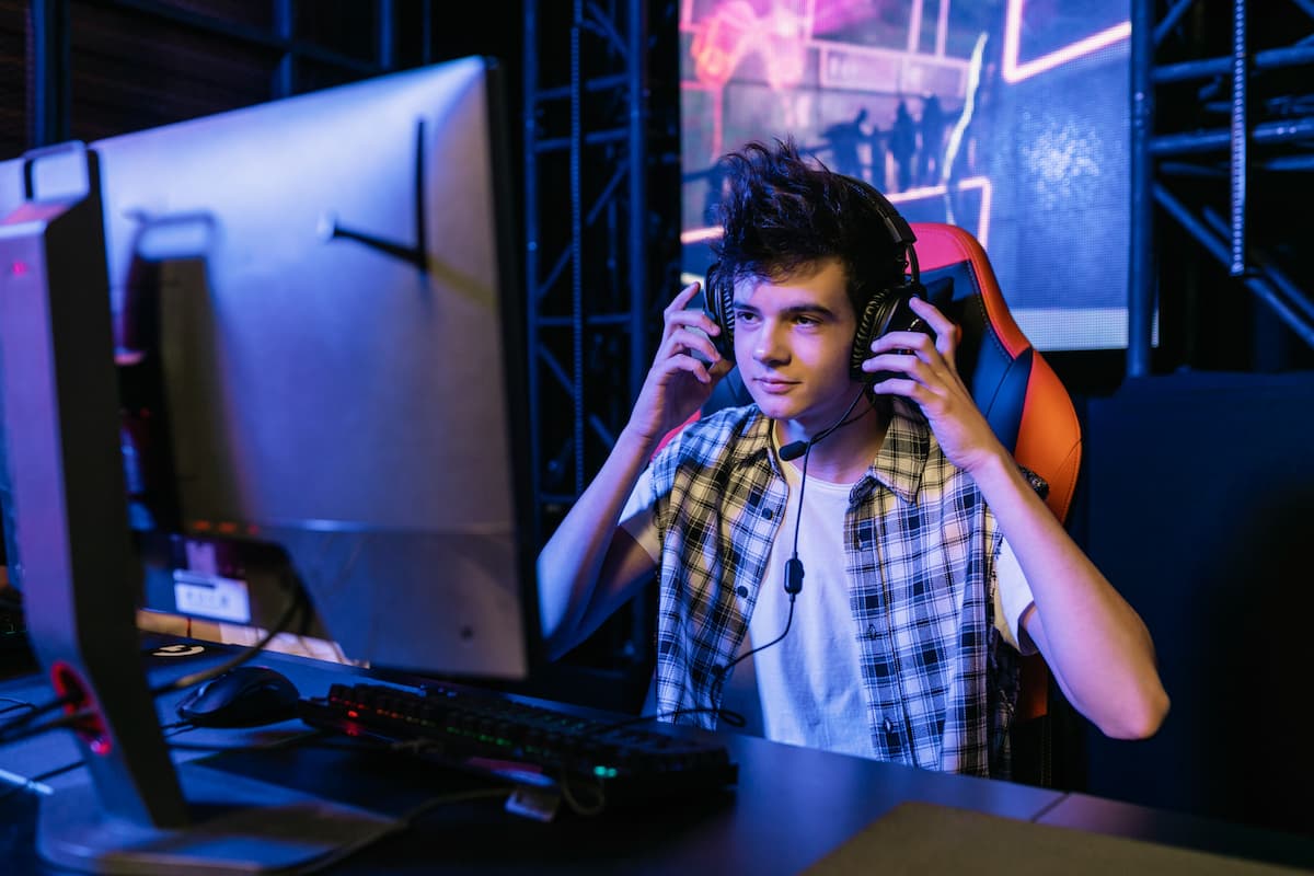 menino na frente do computador com a mão no headset gamer