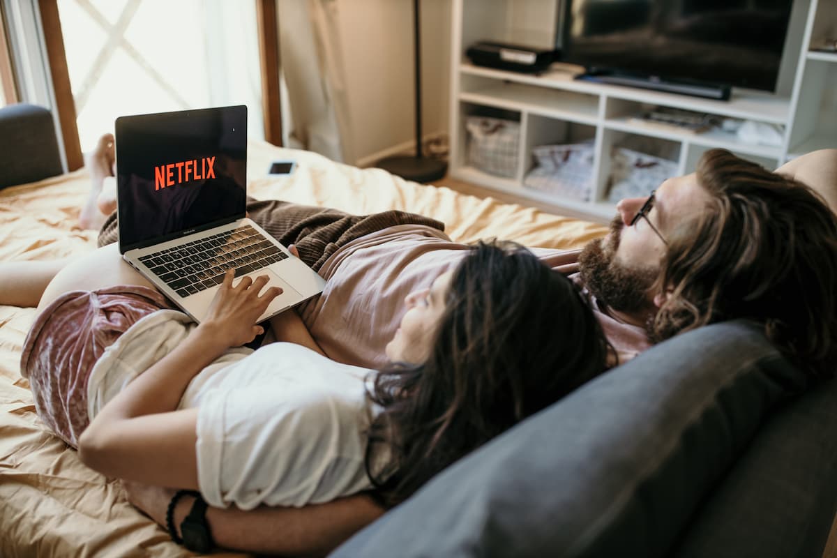 Casal hetero deitado na cama vendo netflix no computador dia dos namorados
