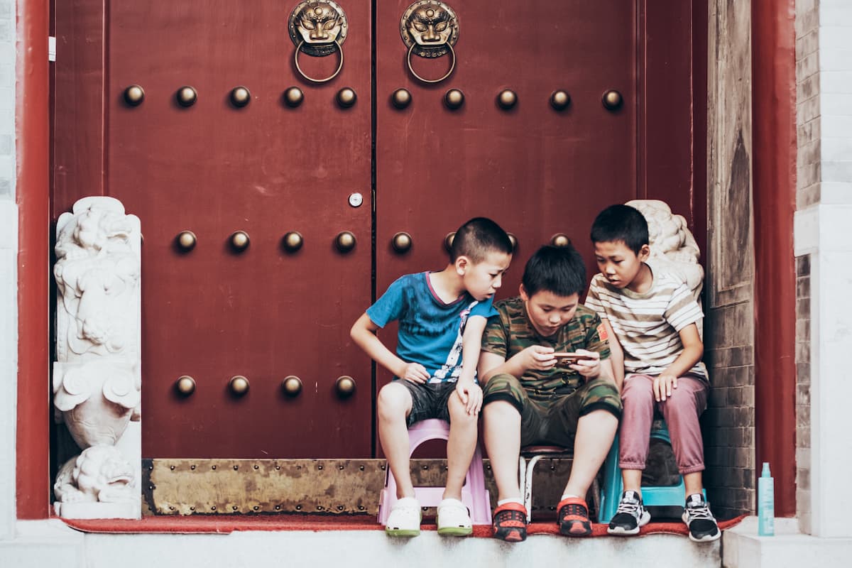 3 crianças jogando em um celular na frente de uma construção