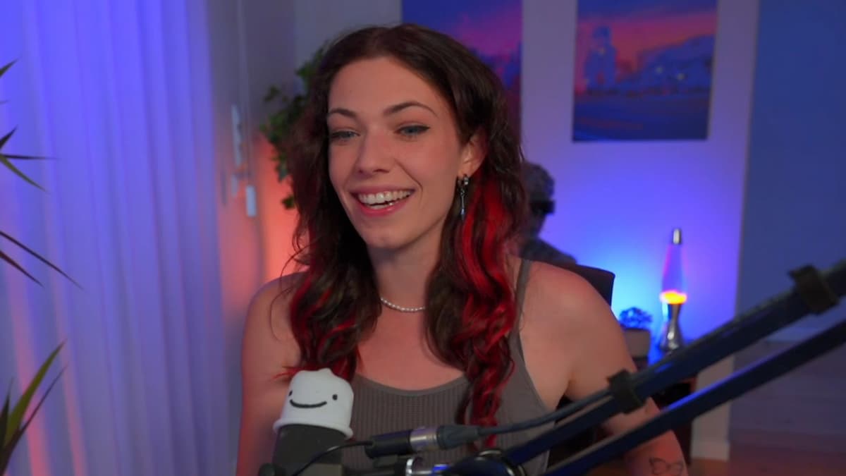streamer da twitch reved, mulher alemã branca com cabelo com mechas vermelhas com microfone na sua frente em quarto iluminado com led azul