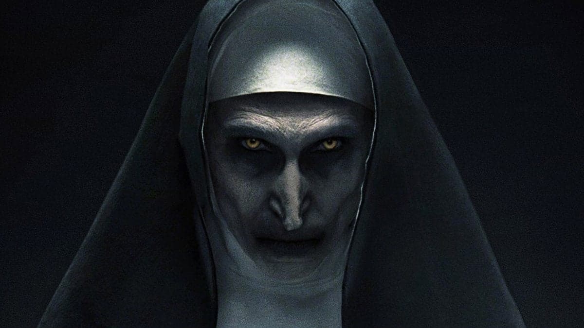 Freira demoníaca do filme A Freira 2 em um ambiente escuro. Seu rosto está parcialmente iluminado, transmitindo um ar sombrio e assustador.