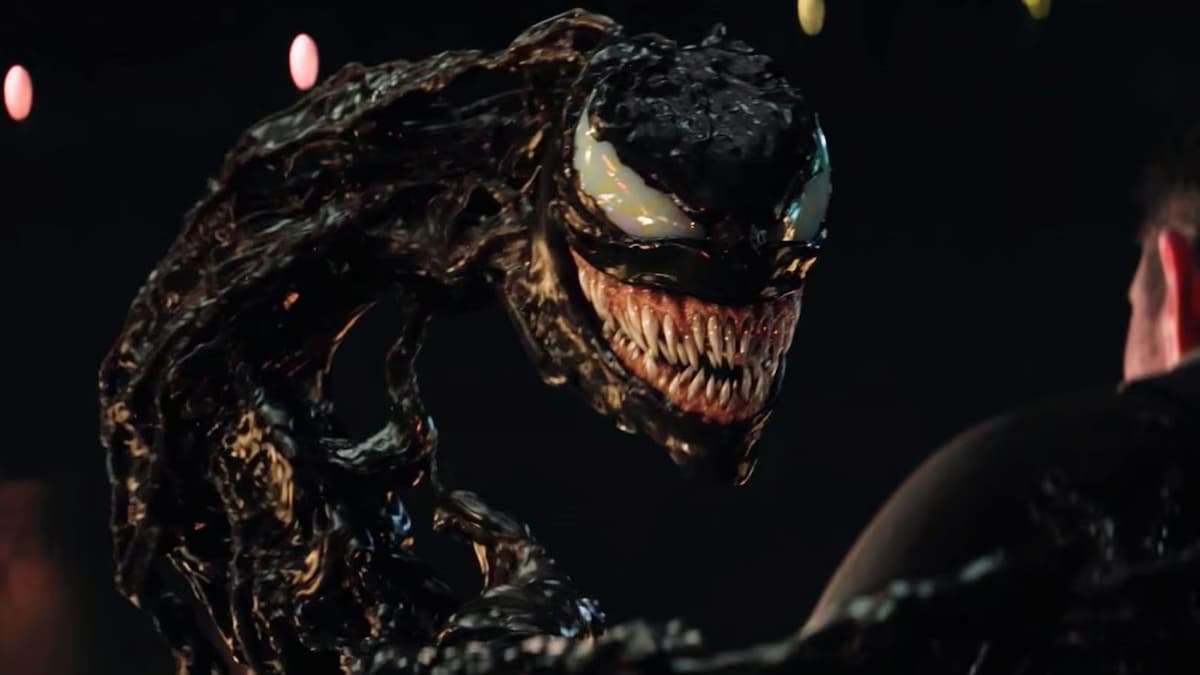 Personagem Venom do filme Venom 3, criatura gosmenta preta com olhos grandes brancos e muitos dentes afiados.