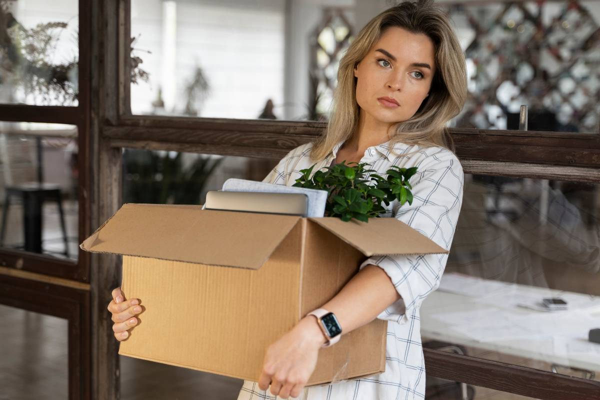 Demissão. Mulher com semblante desanimado segurando uma caixa com seus pertences de escritório após sofrer demissão.