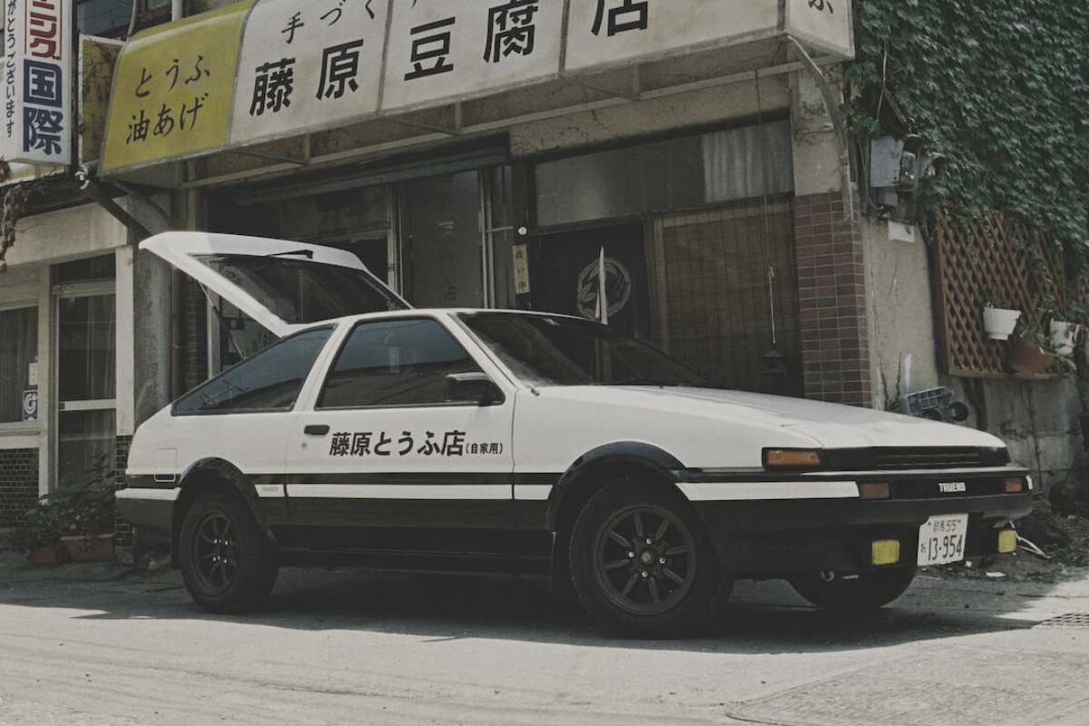 Cena do filme live-action do anime Initial D, nele um carro branco estacionado de lado aparece no centro da imagem.