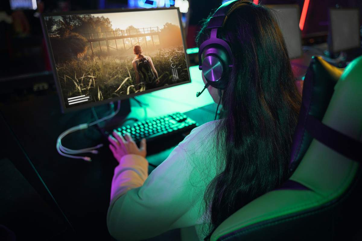 Mulher em alto ângulo usando headphone e se divertindo com jogo em um computador gamer.