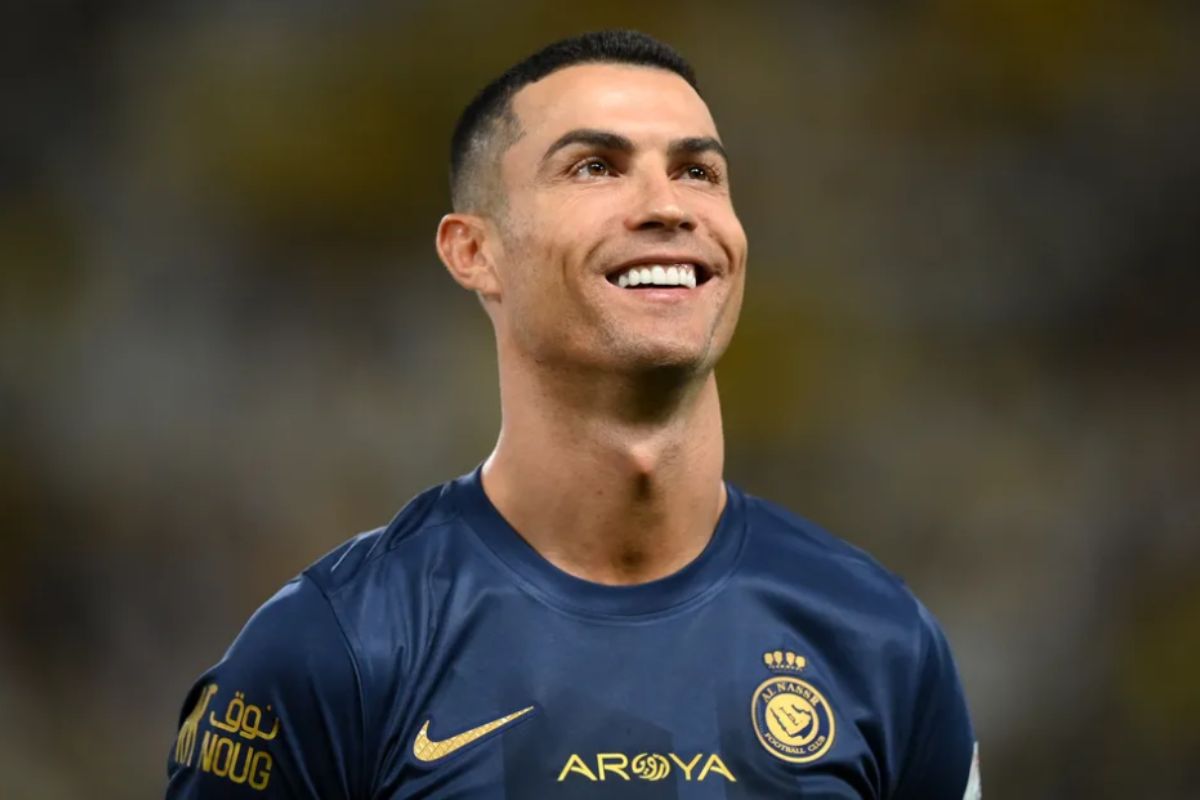 Cristiano Ronaldo uniformizado sorrindo em campo durante jogo de futebol.
