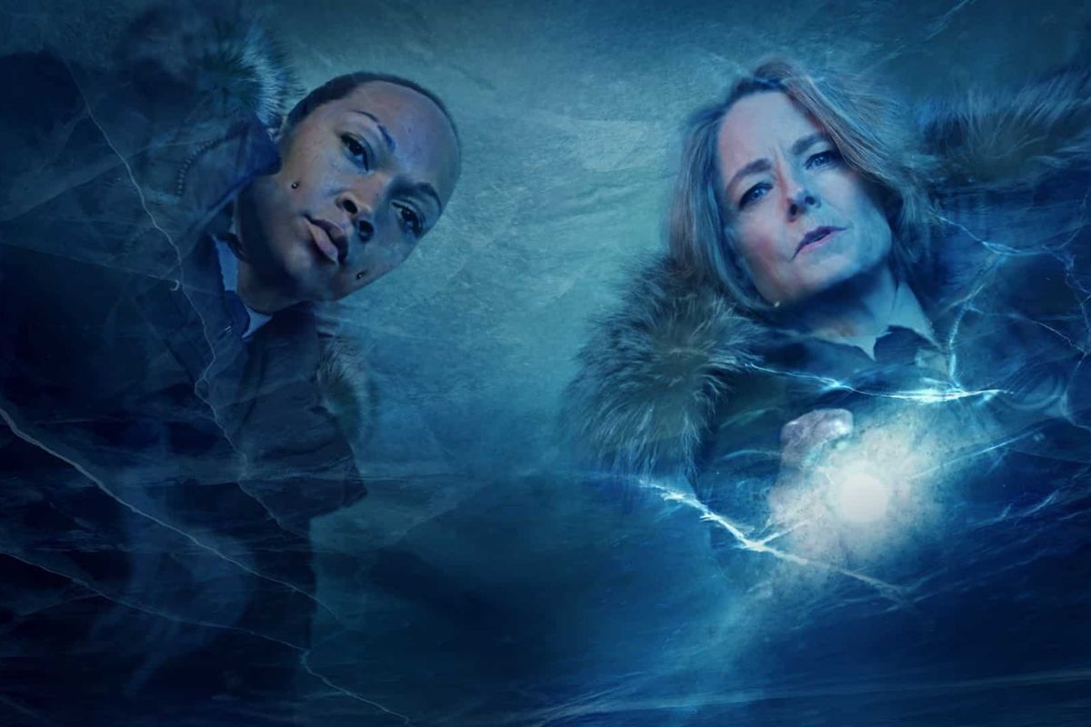 True Detective Terra Noturna. Cena da série True Detective Terra Noturna, na qual as duas protagonistas estão em um ambiente de neve, olhando para baixo, usando roupas de inverno.