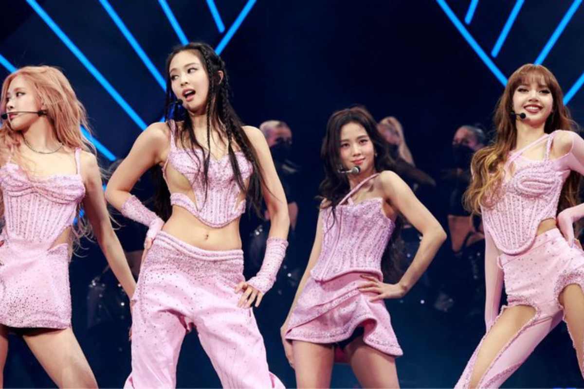Membros do grupo de k-pop Blackpink se apresentando em um palco. Elas estão com roupas cor de rosa e estão posicionadas, da esquerda para a direita, Rosé, Jennie, Jisoo e Lisa.