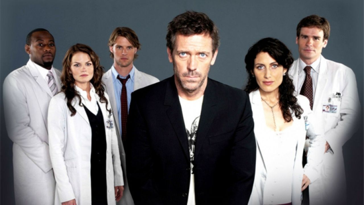 Foto com os atores principais da série House. Dispostos lado a lado, eles vestem jaleco branco. Ao centro, o protagonista Dr House veste m terno preto.